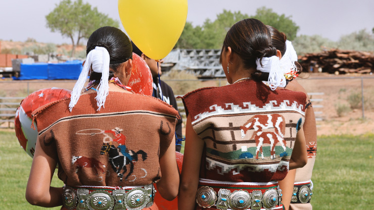 Youth facing away from the camera wearing Navajo traditional hairtie and woven rug tapestry dress and silver and turquoise jewelry.