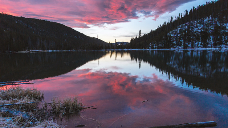Sunrise Over Lake. Red Clouds reflected on a lake, surrounded by wintery mountain range. Some snow and frost cover the ground and grassland areas. 