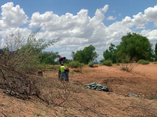 Two people standing on red soil with a pile of rocks nearby talking. Blue sky in background with white clouds. 