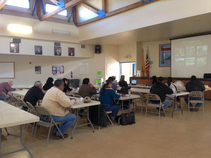 People sitting in table listening to a presentation at a Public Scoping meeting in Fort Defiance, AZ. 