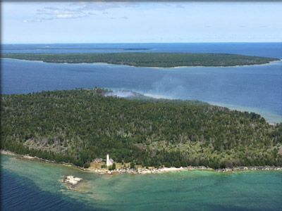 Lighthouse on the 200 ac. Poverty Island is centered on the southern end of the Island while a small smoke column is visible on the other side of the island, north of the structures.