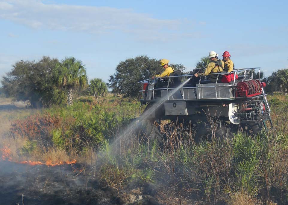Firefighters extinguish flames from a swamp buggy. An engine boss trainee provides oversight as part