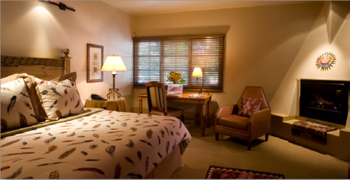 Hotel room featured in soft light with a queen bed, desk and fireplace.