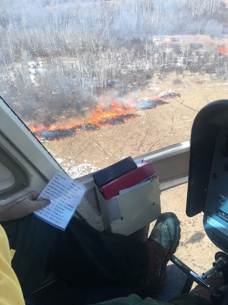 Red Lake Helitack crew members drop plastic spheres containing potassium permanganate from the helicopter. This is noticeable by the circular burn patter of the fire below. Photo by: Red Lake Fire Management