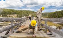 Interior employees building a bridge while one person is hammering a nail into a piece of wood. 