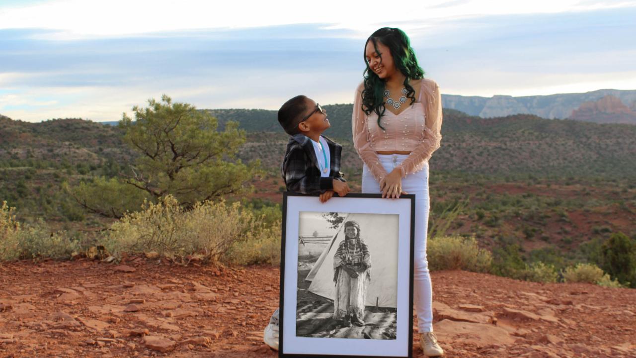 A photo of a young boy and girl holding a portrait of their relative. 