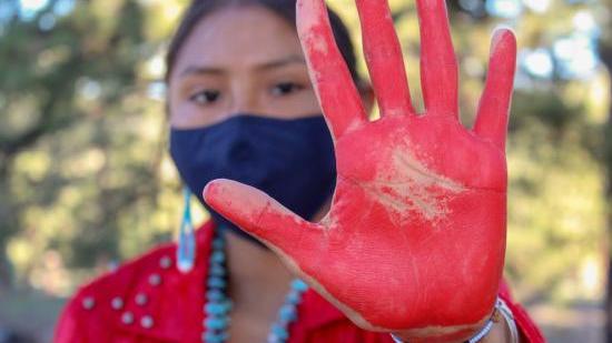 Photo of a Native American woman with a red handprint in the forefront of the photo.