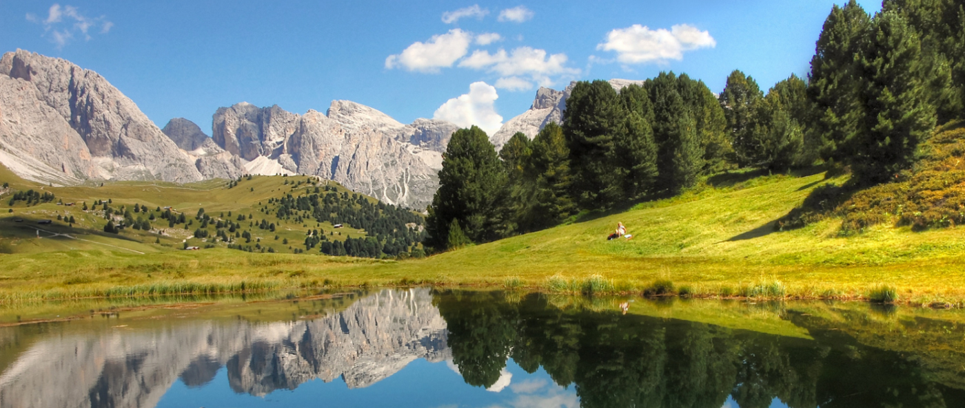 A placid lake reflects the stony mountains and trees in the landscape.