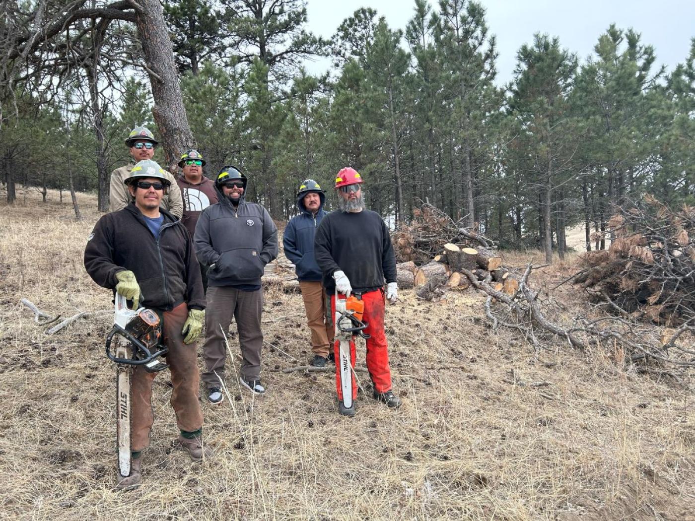 Six wildland firefighters outside on the Oglala Sioux Reservation. Two men are holding chainsaws.