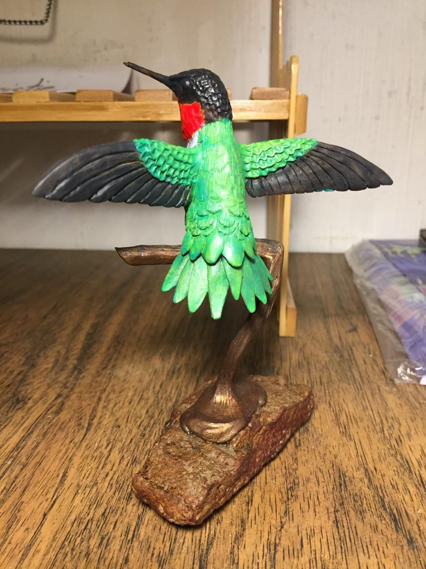 Sculpture of a perched green hummingbird with wings outstretched. 