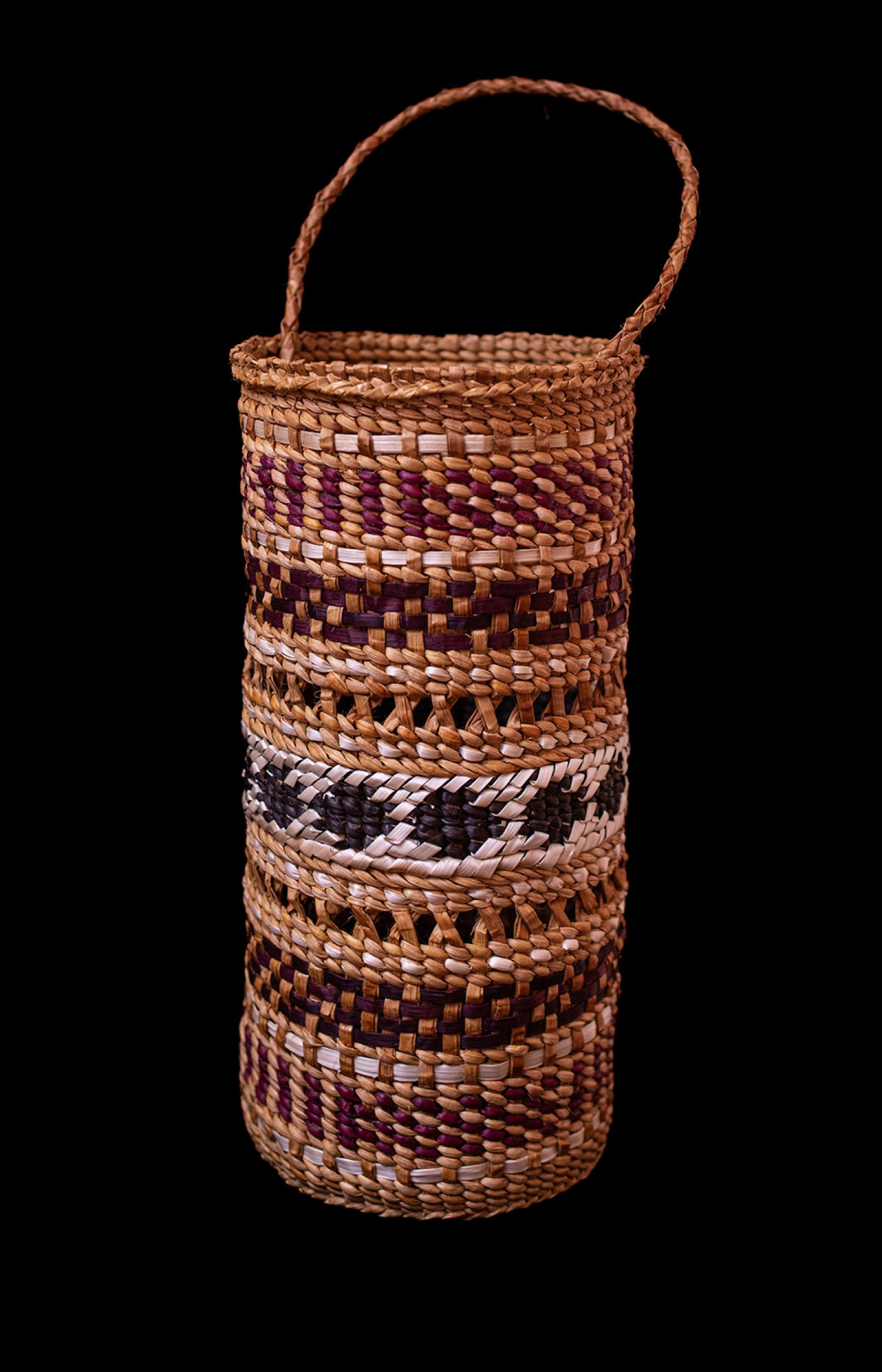 Photograph of a woven cedar bark basket. The basket is tall and narrow with 5 bands of woven patterns.