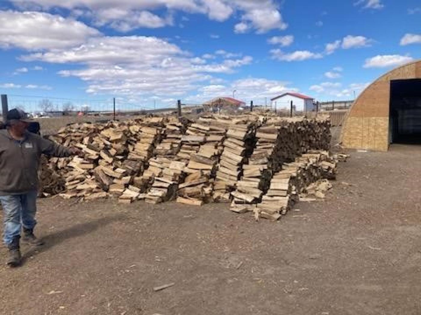 A tribal employee worker showing a big pile of wood at an outside yard.