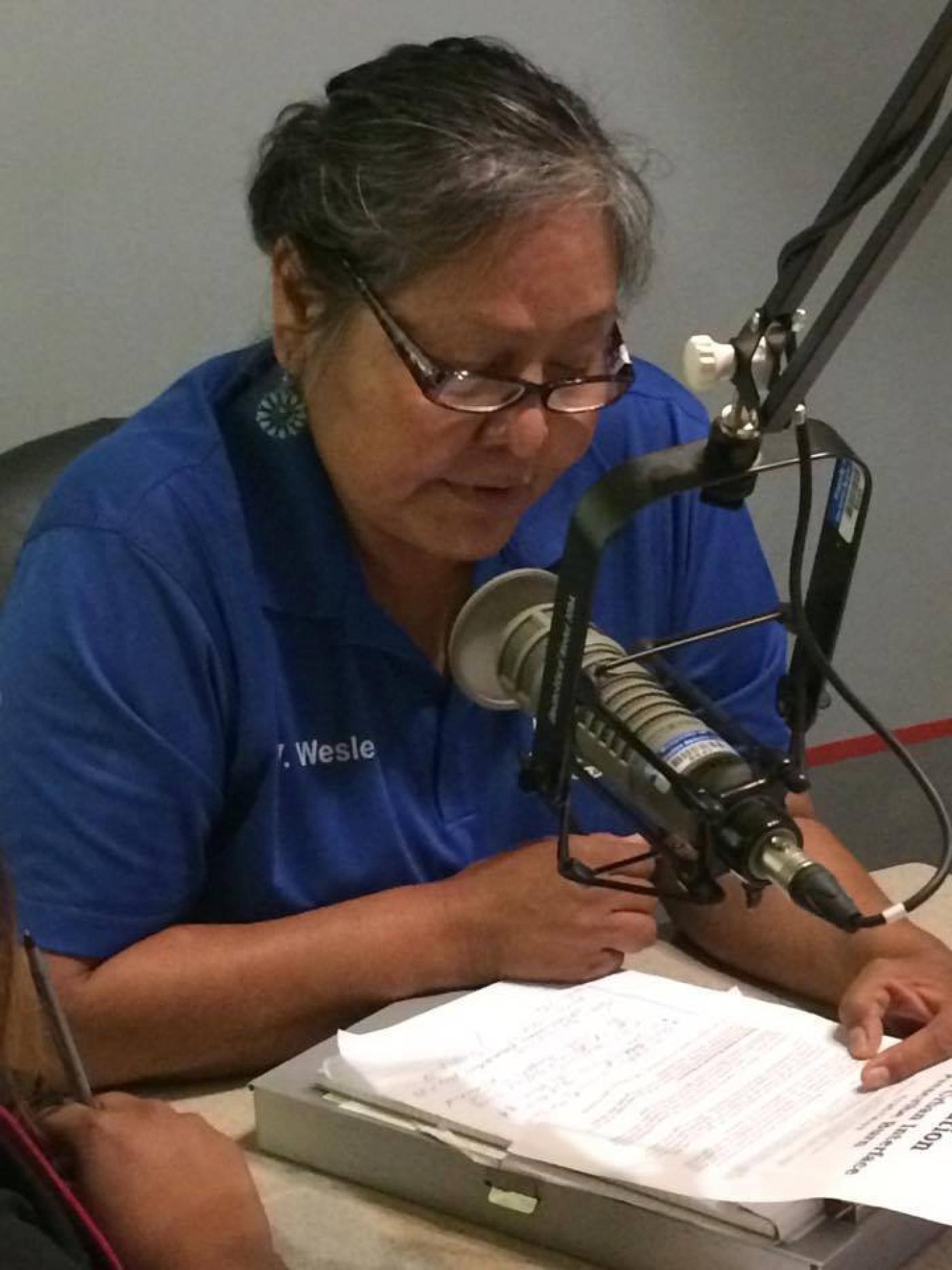 A public information officer speaks into a microphone while consulting a list of questions for a radio interview.